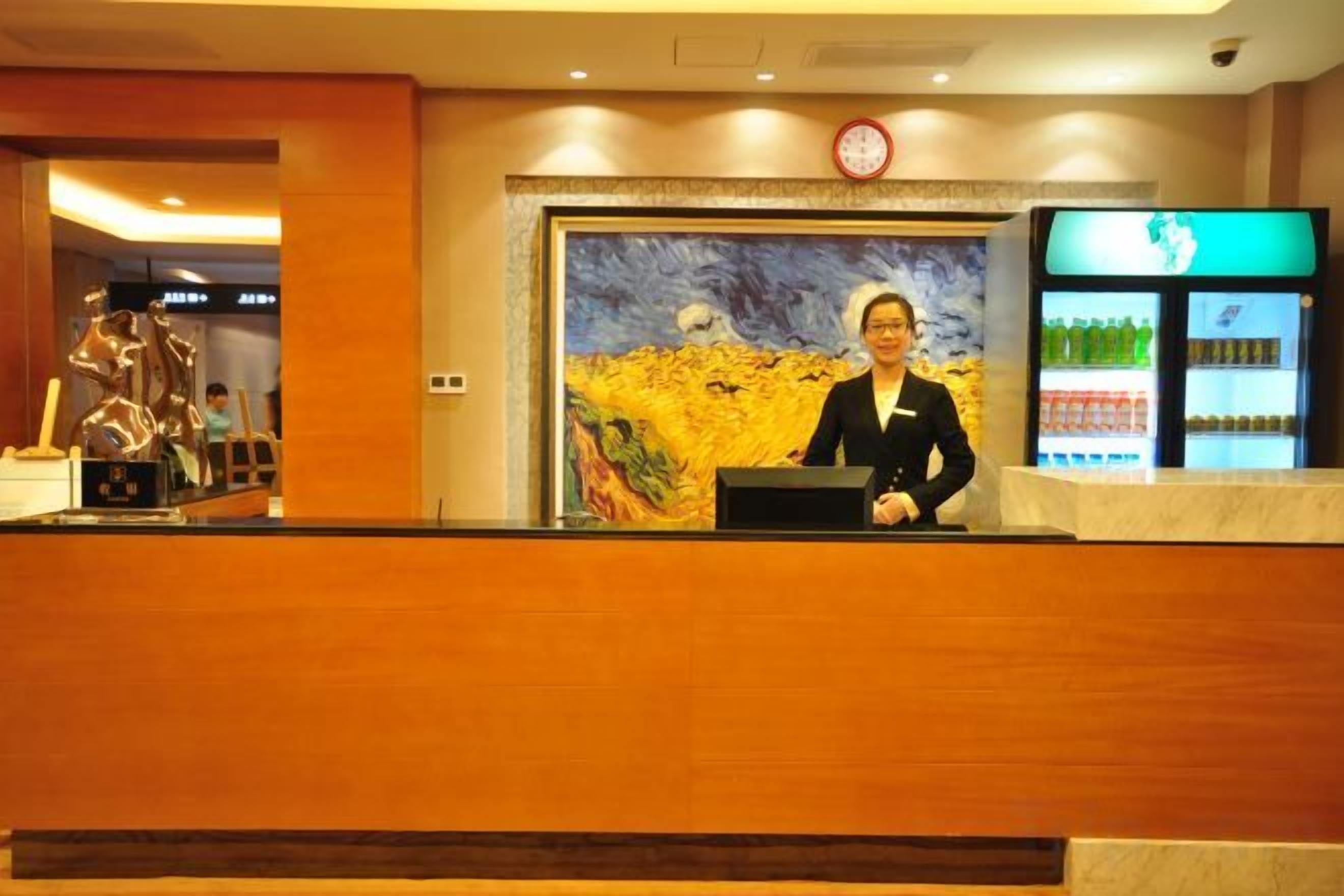 A reception desk with a clock above it, a painting on the wall, and a refrigerator with beverages.