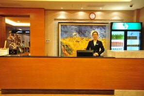 A reception desk with a clock above it, a painting on the wall, and a refrigerator with beverages. - Green Bin Phoenix Hotel(Beiliu Country Garden ) (Beiliu)