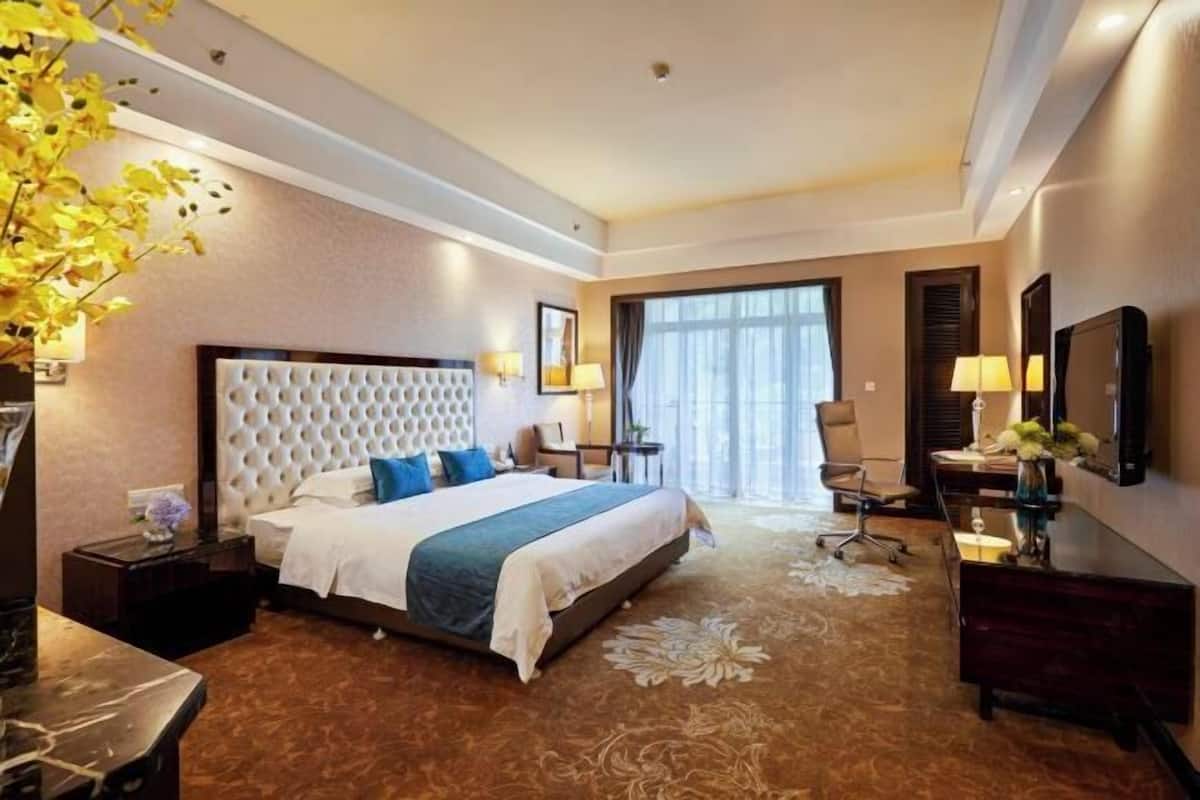 A hotel room with a large bed, a desk, a chair, and a window with curtains.