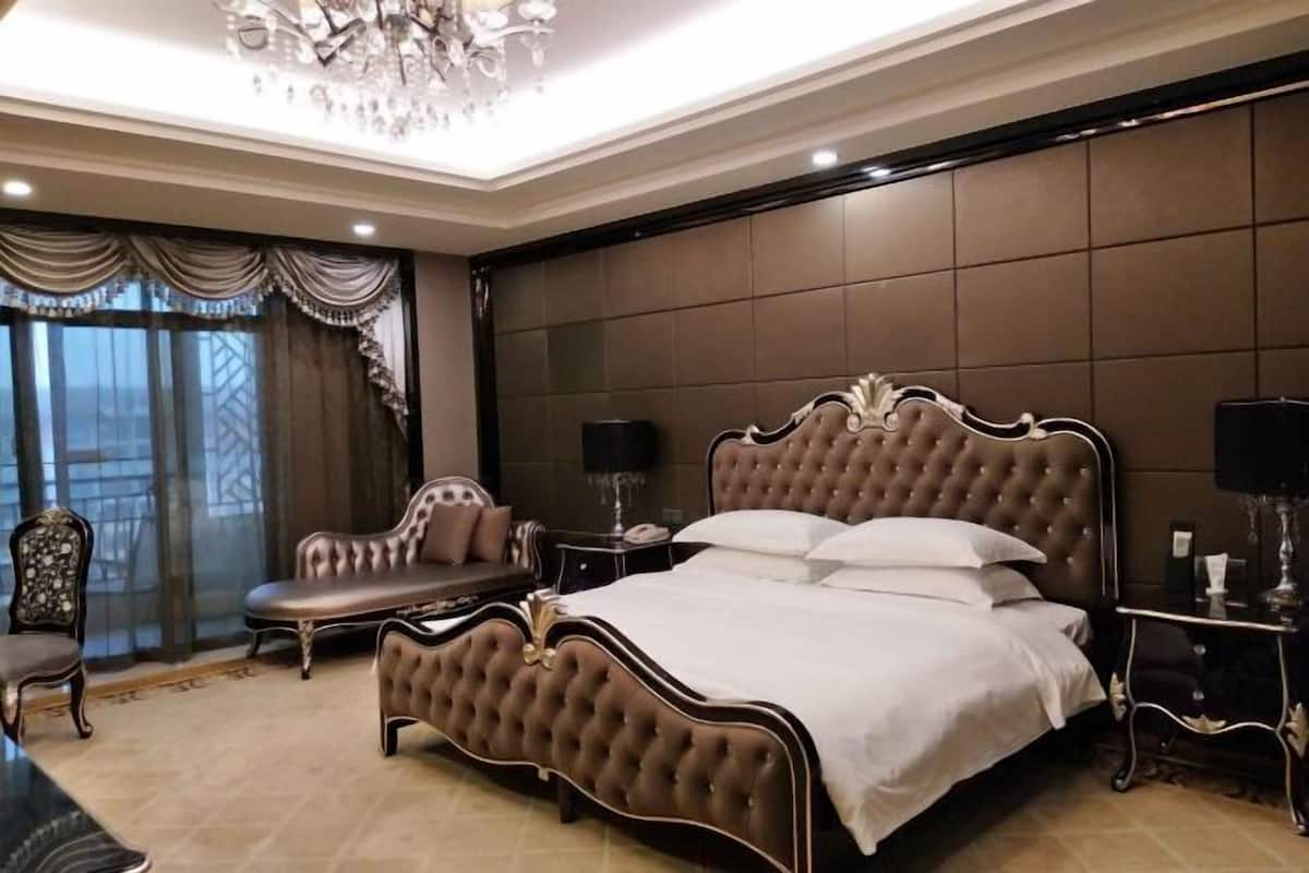 A bedroom with a large bed, a chandelier, a sofa, and a television.