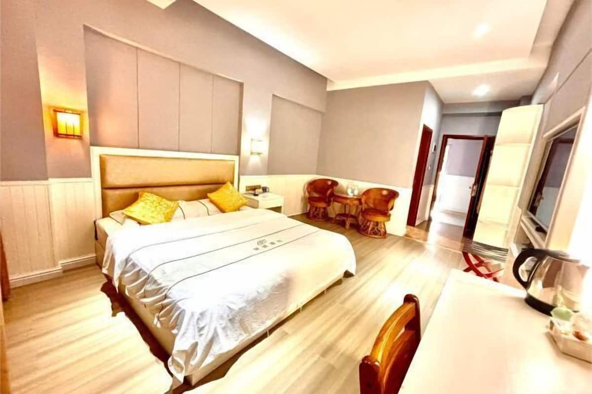 A hotel room with a large bed, a desk with a chair, a television, and a small table with a kettle.