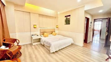 A hotel room with a bed, bedside table, lamp, and a seating area with chairs.