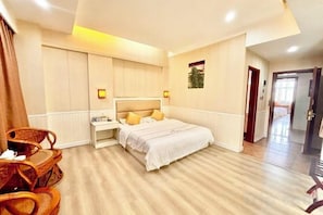 A hotel room with a bed, bedside table, lamp, and a seating area with chairs.