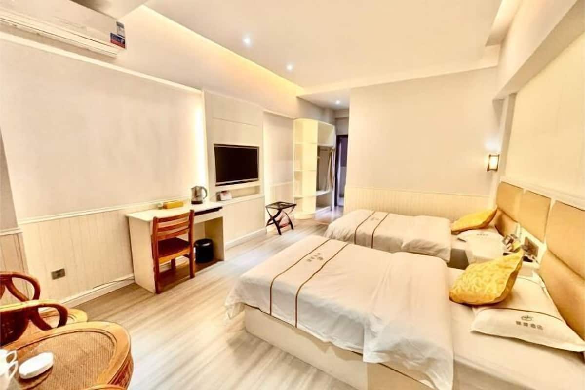 A hotel room with two beds, a desk, a chair, a television, and a small table.