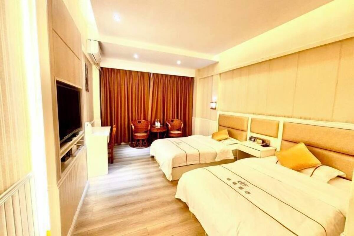 A hotel room with two beds, a TV, a desk, and a seating area with chairs.