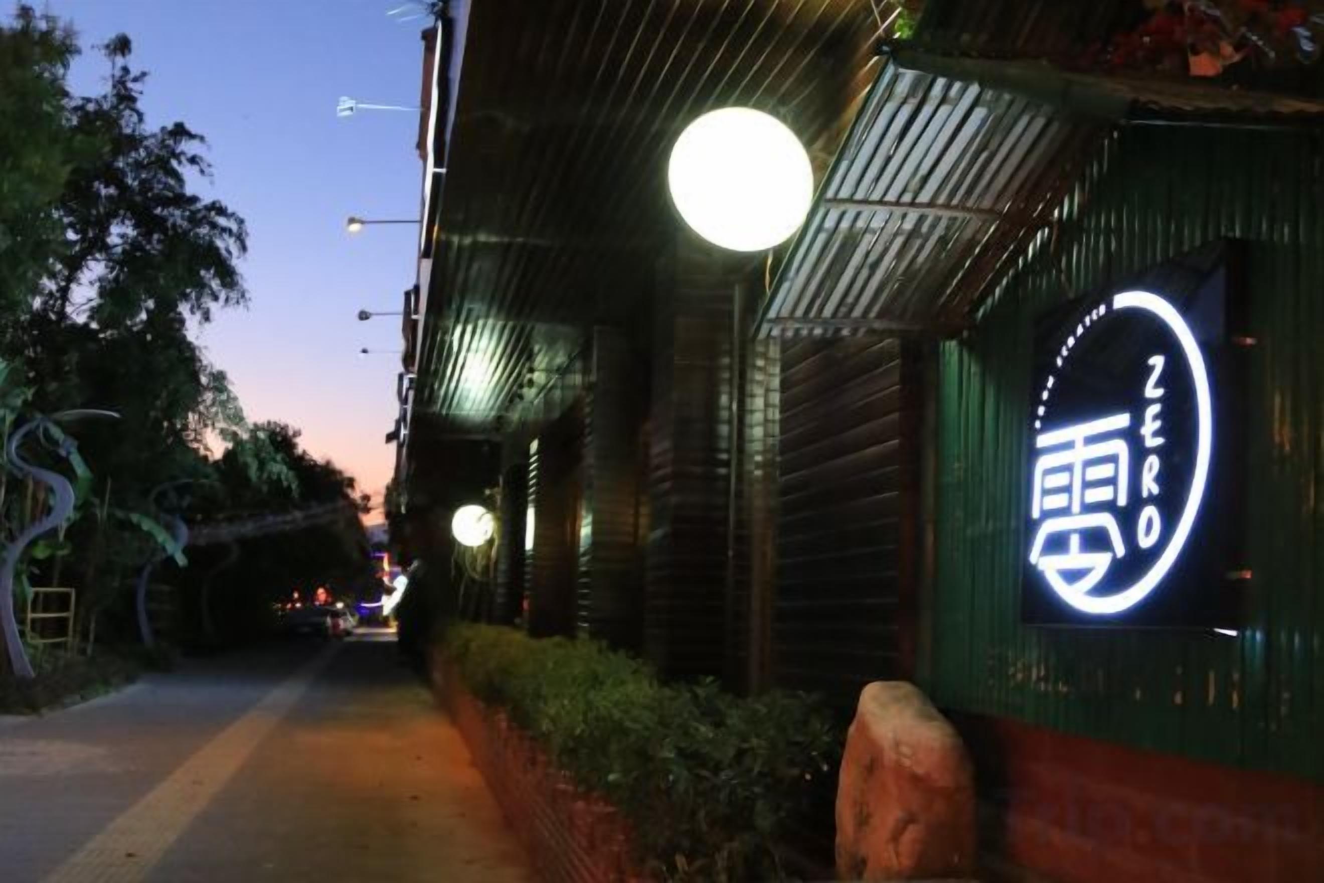 A street view with a restaurant named 'ZERO' with a neon sign, a sidewalk, and street lamps.