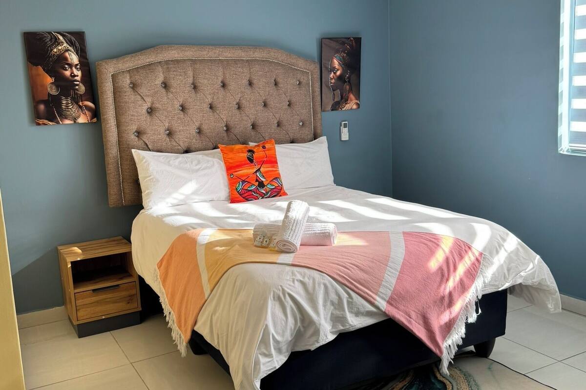 Une chambre à coucher avec une tête de lit capitonnée, un lit avec une literie blanche et rose, une petite table de chevet en bois et un tapis à motifs de marbre.