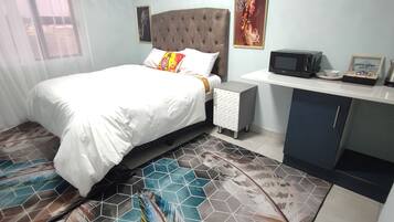A hotel room with a bed, a small desk, a microwave, and a kettle.
