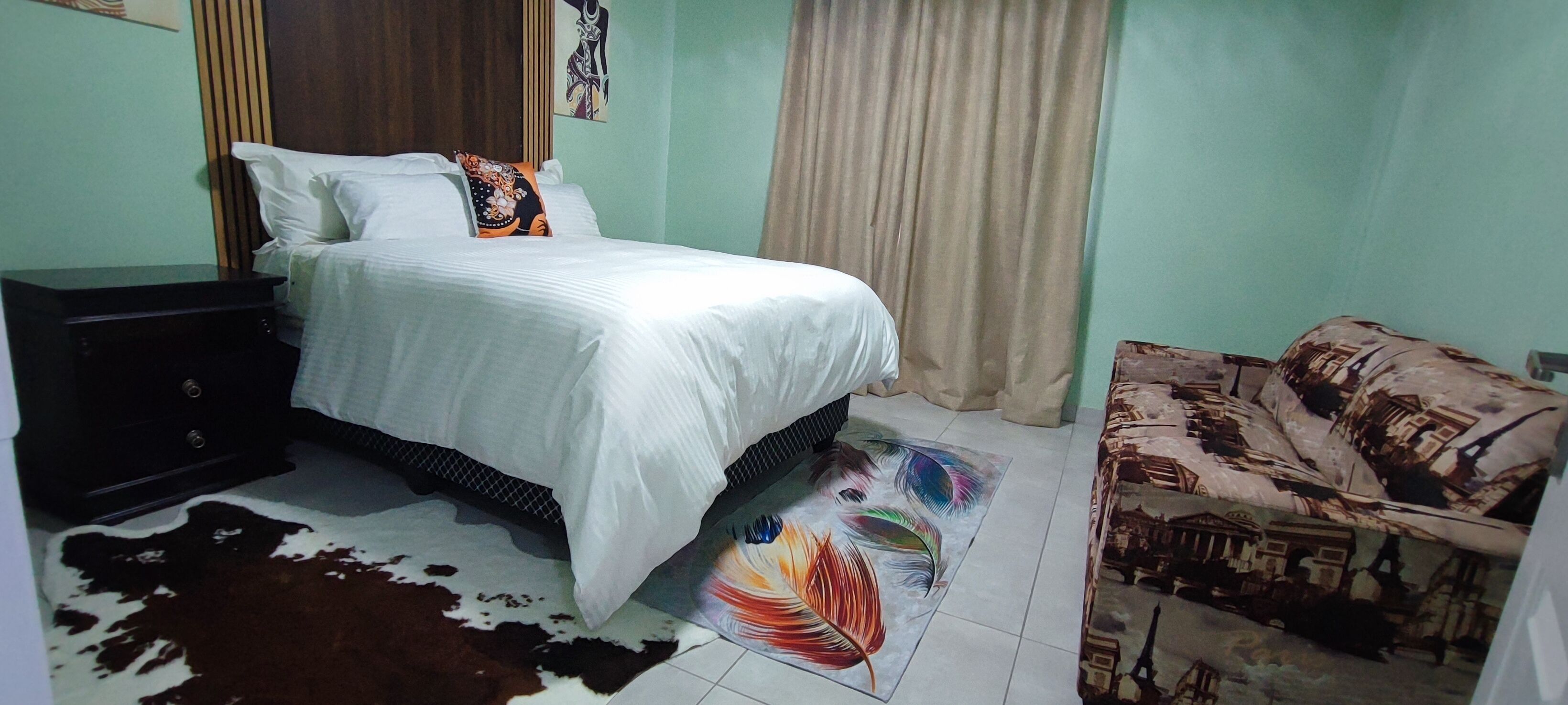 Un dormitorio con cama, mesita de noche, alfombra de cuero de vaca, alfombra colorida y sofá con diseño de paisaje urbano.