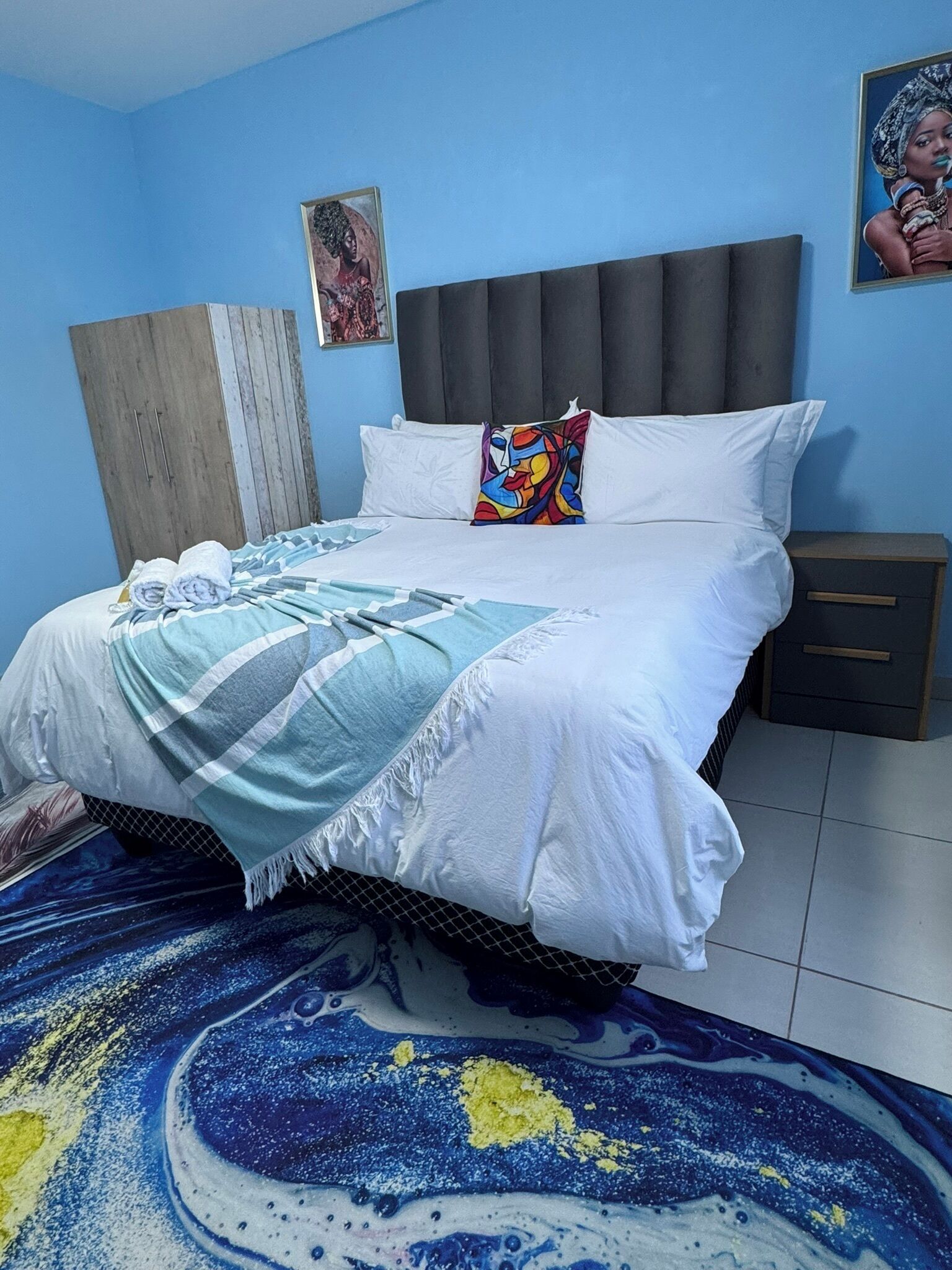 A bedroom with a bed, a nightstand, a wardrobe, and a colorful rug.