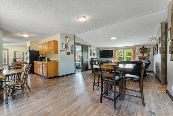 A spacious kitchen with wooden cabinets, a dining area with a large table and chairs, and a living area with a sofa and TV. - Pet friendly 4 bed 2 bath home with outdoor shower close to local campgrounds! (Pineville)