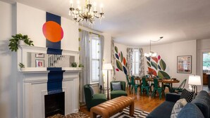 Ein modernes Wohnzimmer mit Kamin, grünen Sesseln, einem blauen Sofa und einem Essbereich mit einer Chandelier.