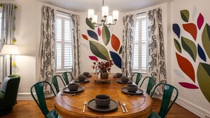 Ein Esszimmer mit einem runden Holztisch, grünen Stühlen und einer Vase mit Blumen.