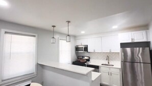 A modern kitchen with white cabinets, stainless steel appliances, and pendant lighting.