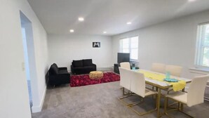 A modern living room with a black sofa, a red rug, and a dining area with a yellow tablecloth.