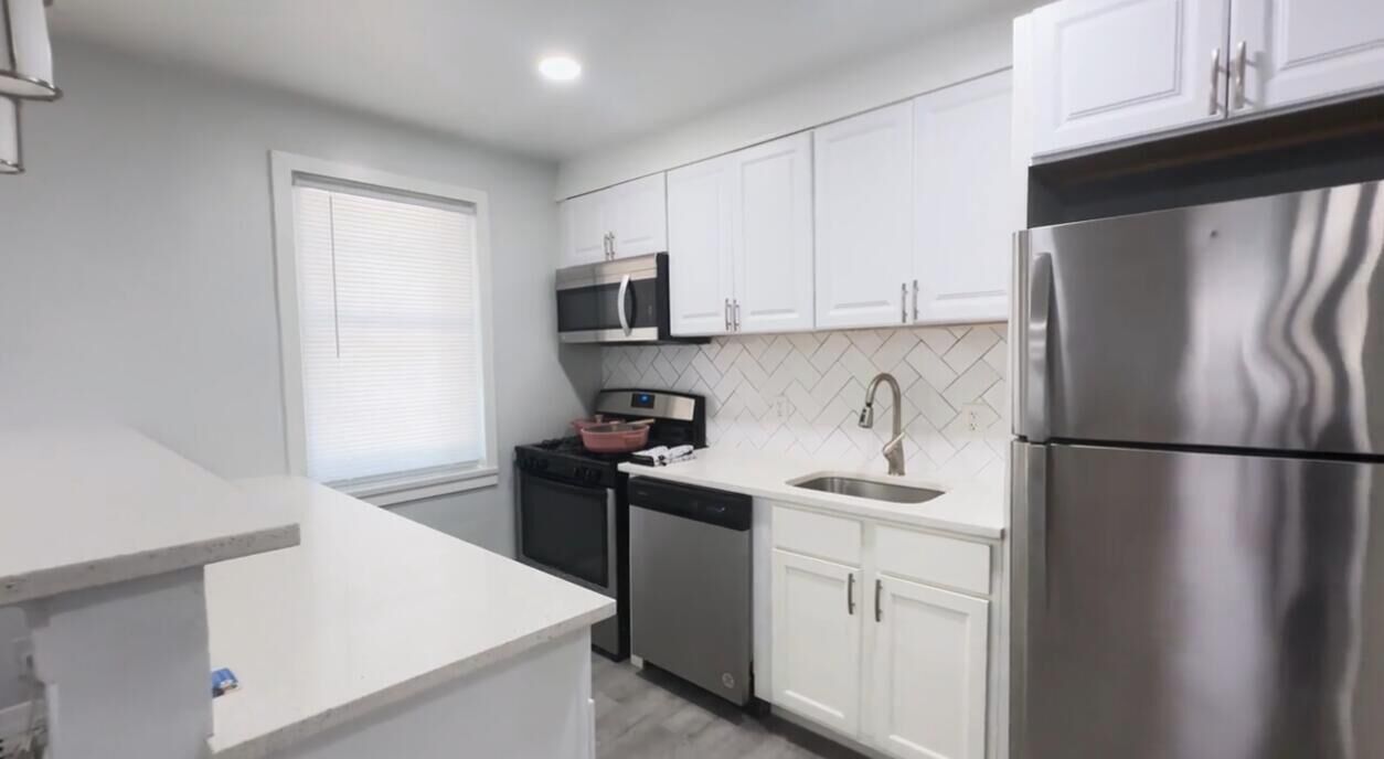 A modern kitchen with white cabinetry, stainless steel appliances, and a built-in oven.