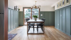 A dining area with a wooden table and chairs, a potted plant, and a view through a glass door.
