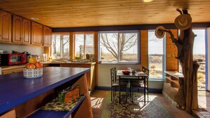 Une cuisine avec des meubles de rangement en bois, un plan de travail bleu et un coin repas comprenant une table et des chaises.