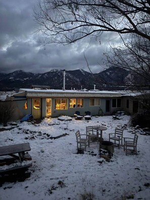 A house with a snow-covered yard, outdoor seating, and a mountain backdrop. - Earthship Stunning Views (Saguache County)