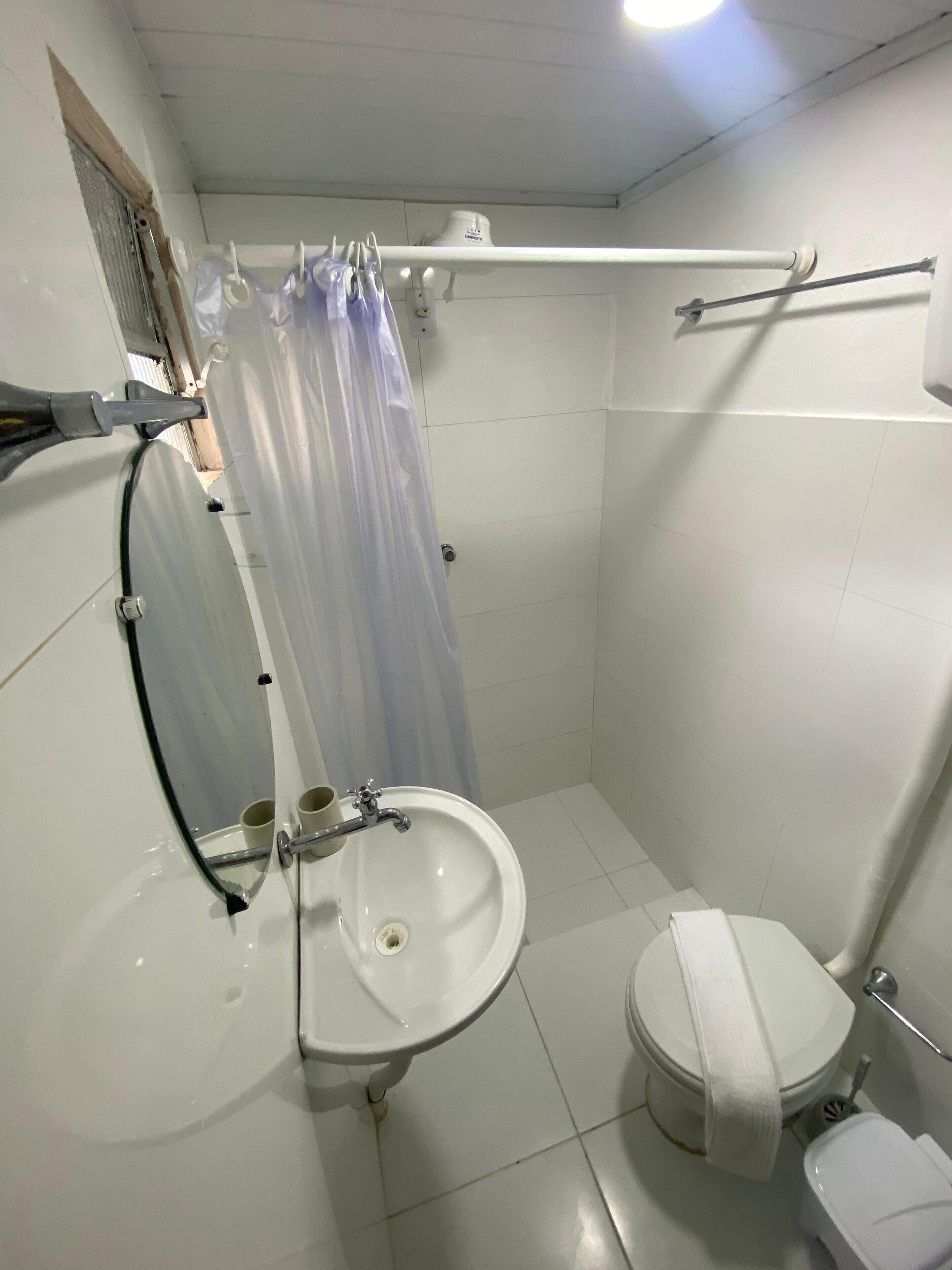 A small, white bathroom with a sink, toilet, and shower curtain.