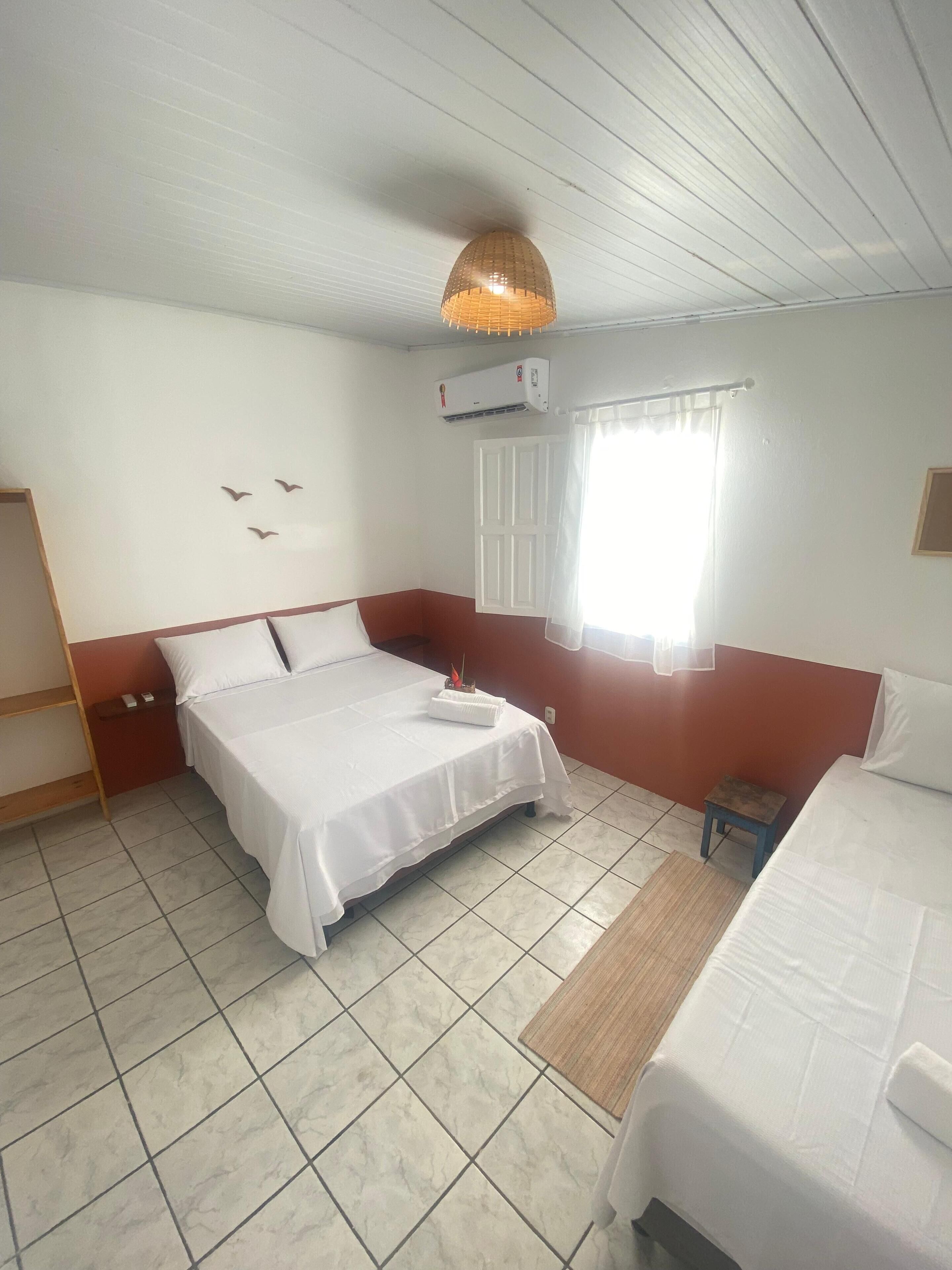 Una habitación con una cama, una mesita, un estante y un aire acondicionado.