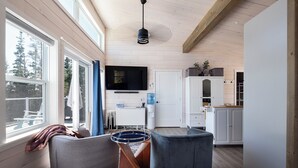 A spacious living area with a large window, a flat-screen TV, and a kitchen with white cabinets.