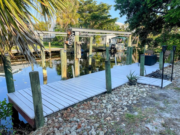 A wooden dock extending over a body of water, with a small outdoor seating area and a gazebo-like structure in the background.