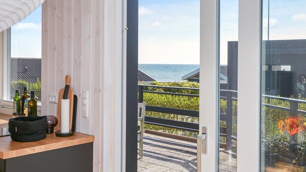 A balcony with a view of the sea, a wooden counter with bottles and a knife, and a door leading to the outside. - Amazing home in Juelsminde (Juelsminde)