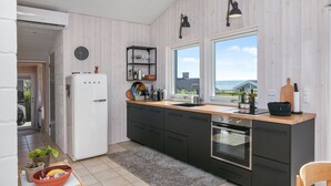 A modern kitchen with a white refrigerator, black cabinets, a wooden countertop, a built-in oven, and a window with a view of the sea. - Amazing home in Juelsminde (Juelsminde)