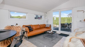 A cozy room with a leather sofa, a small round table, and a chair. There is a large window and a sliding glass door leading to an outdoor area. - Amazing home in Juelsminde (Juelsminde)