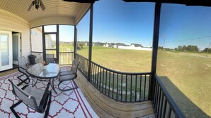 A covered porch with a glass door, a table with chairs, and a view of a grassy field and houses in the distance.