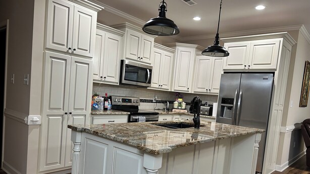 A kitchen with white cabinetry, granite countertops, stainless steel appliances, and a wooden floor.