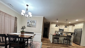 A modern kitchen with white cabinets, stainless steel appliances, and a wooden dining area with a rug.