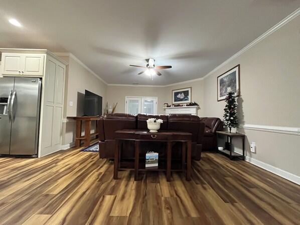 A spacious living room with a brown leather sofa, a wooden coffee table, and a ceiling fan.