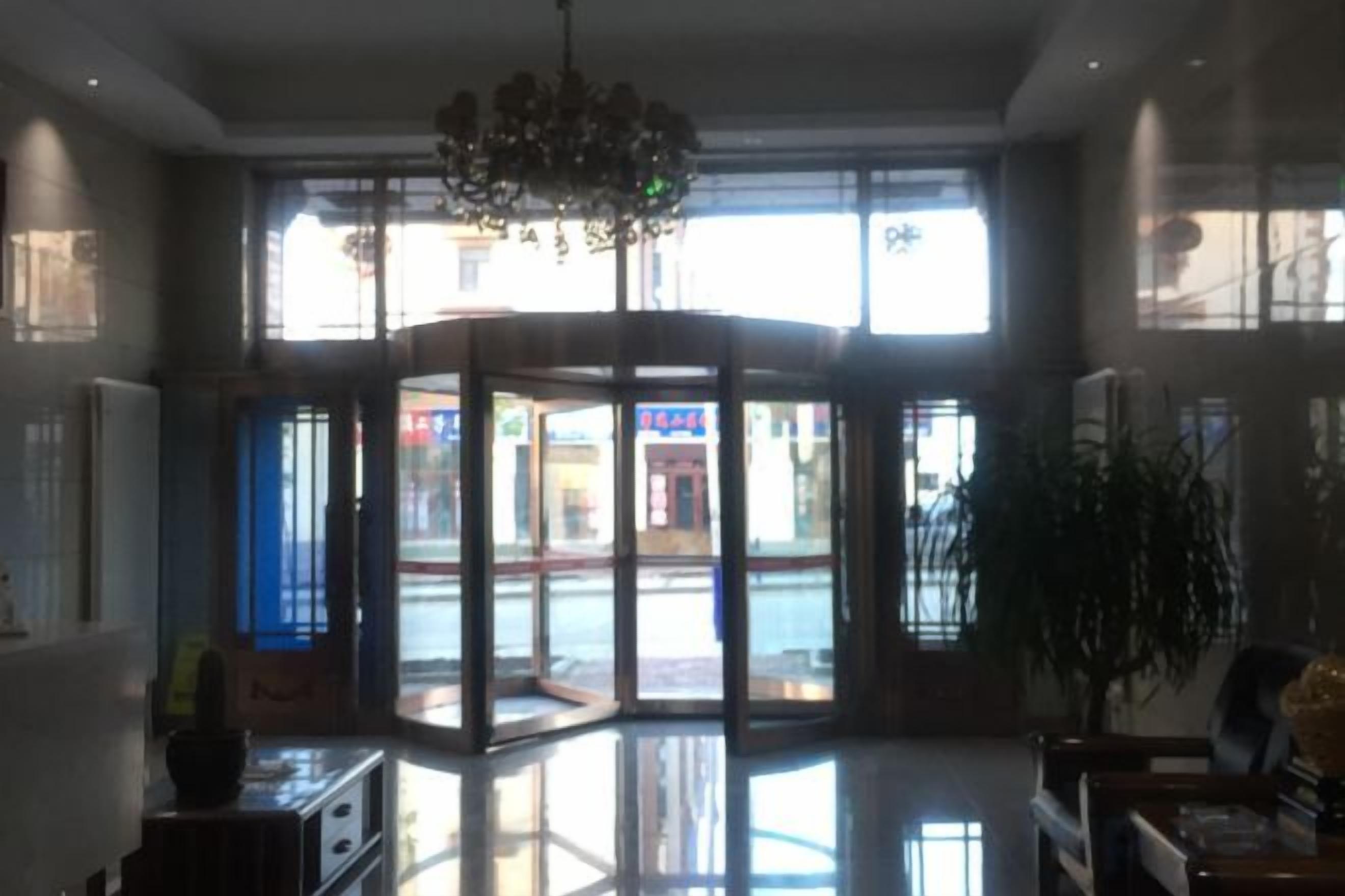 A lobby with a revolving door, a chandelier, and a large window offering a view of the street.