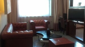 Een woonkamer met een bruine leren bank, een bijzettafeltje en een televisie op een meubel.