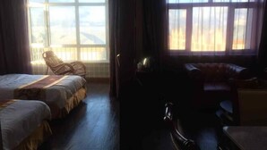 Een hotelkamer met twee bedden, een stoel, een bureau en grote ramen met gordijnen.