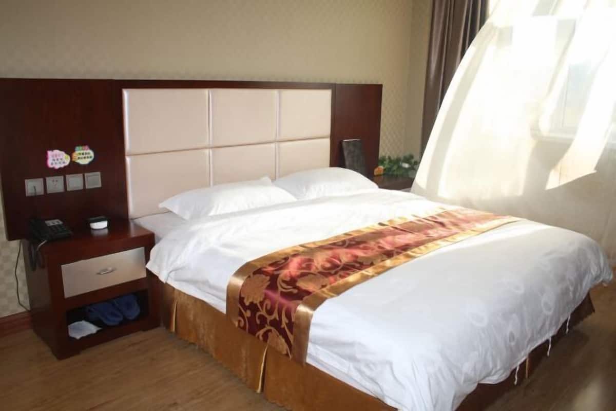 Une chambre d’hôtel avec un lit, une table de chevet avec un téléphone et une lampe, et une fenêtre avec des rideaux.