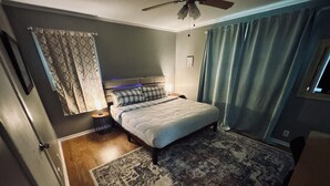 A bedroom with a bed, a nightstand, a ceiling fan, a patterned rug, and a window with curtains. - Charming 4-bedroom house with AC and WiFi in peaceful Texarkana (Texarkana)
