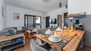 Un salon moderne avec une table à manger en bois pour quatre personnes, un canapé gris et un téléviseur à écran plat fixé au mur.