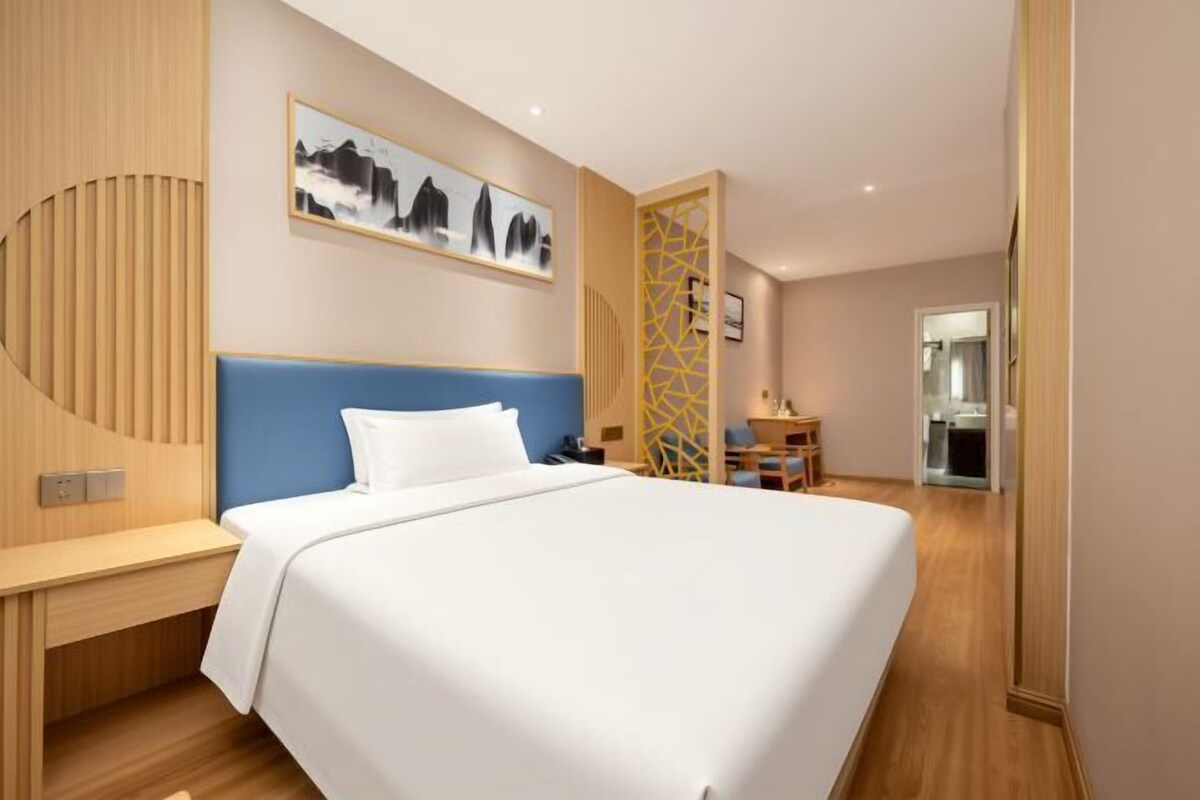 A hotel room with a large bed, a wooden headboard, a desk, and a chair.