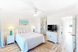A bedroom with a bed, nightstands, a TV, and a ceiling fan.