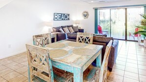 En matplats med ett rustikt träbord och stolar, en soffa och en skylt med texten ”STRAND” på väggen.