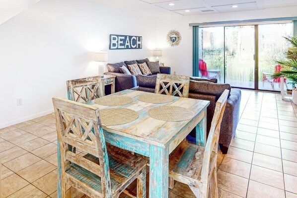 A dining area with a rustic wooden table and chairs, a sofa, and a 'BEACH' sign on the wall.