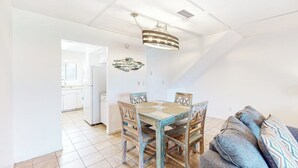 En matplats med ett träbord och stolar, en hängande lampa och utsikt in i köket.