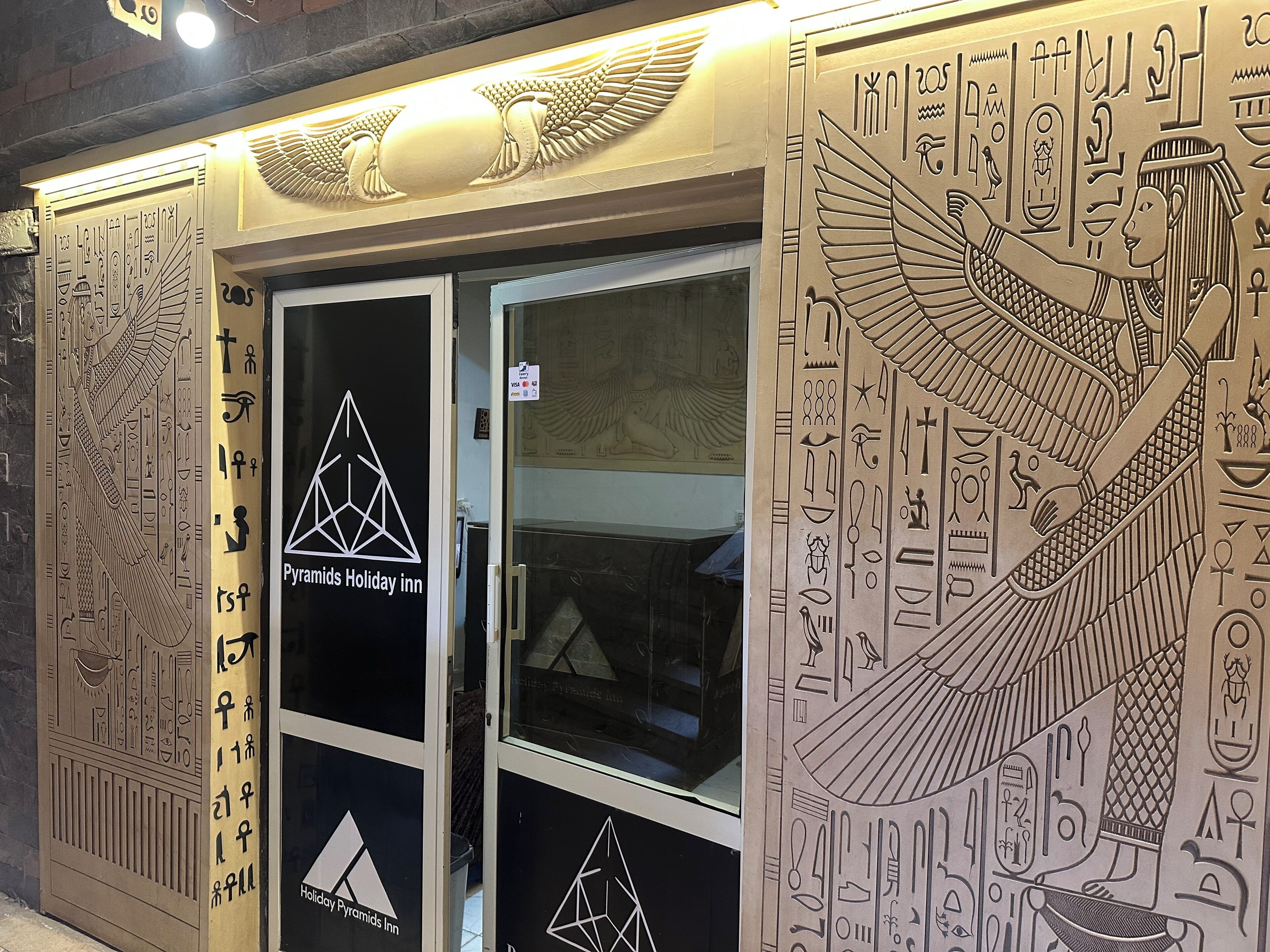 The exterior of the Pyramids Holiday Inn with Egyptian-themed wall art and hieroglyphics.