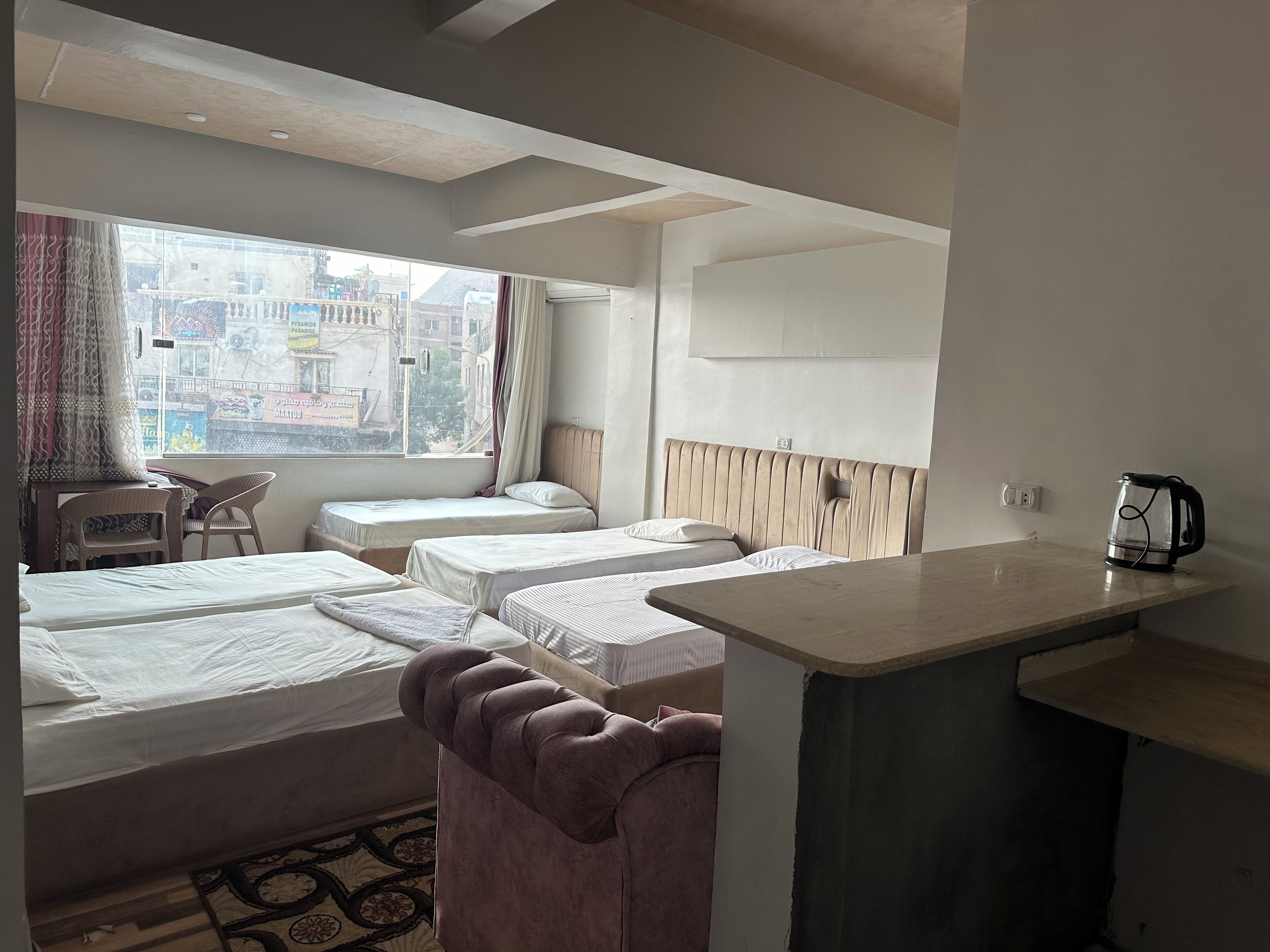 Habitación de hotel con dos camas individuales, un pequeño sofá, kitchenette y vistas a la ciudad.