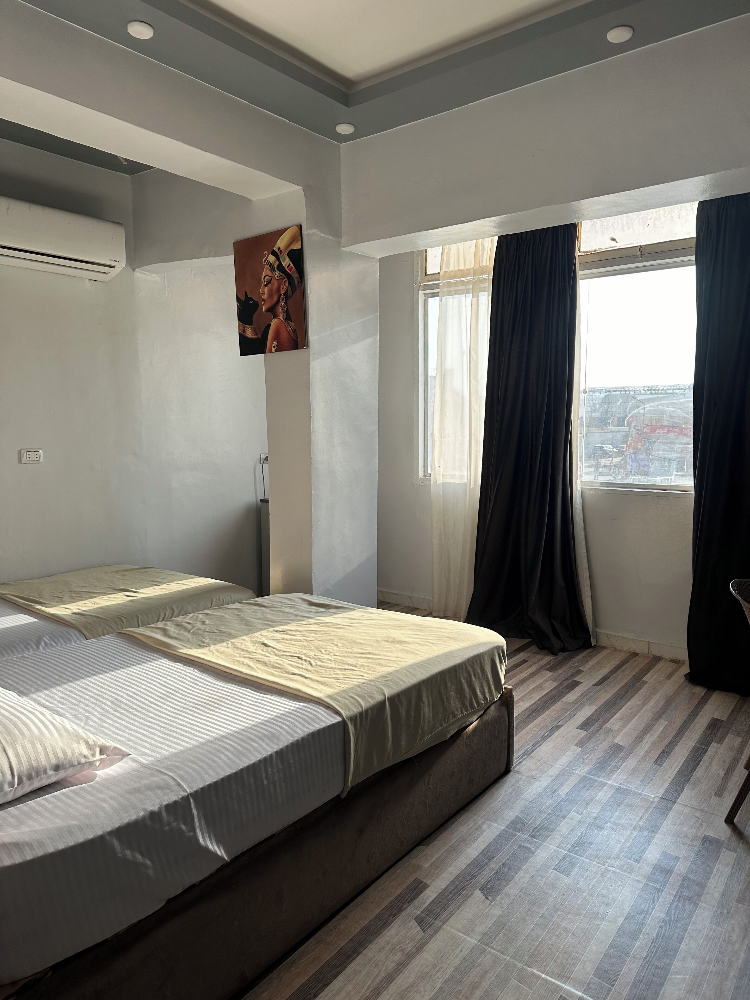 Una habitación de hotel con una cama, un ventanal con cortinas, un aire acondicionado de pared y un cartel.