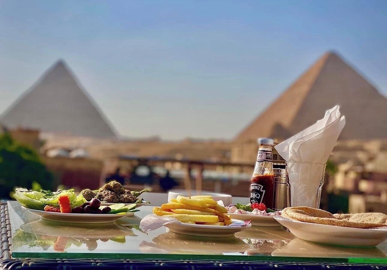 A table with food and drinks, with pyramids in the background.
