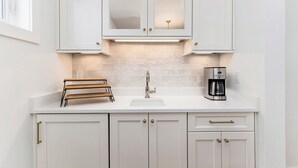 A kitchen with white cabinets, a sink, a coffee maker, and a window. - Luxe Lakefront Living on Stunning Crystal Lake in Benzonia, MI (Benzonia)